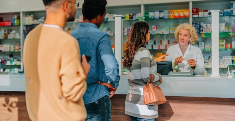 A couple of diverse people are standing in the queue at the pharmacy, waiting for their turn.